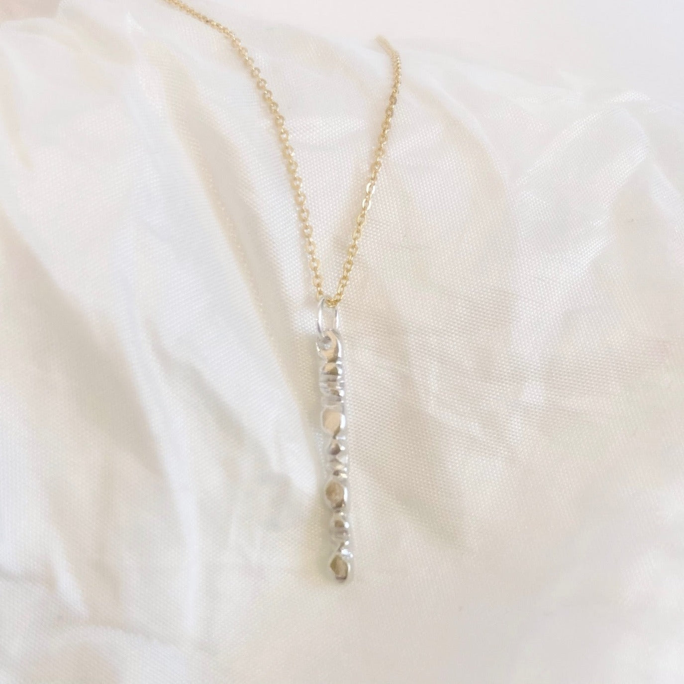 A beautiful mixed metals piece. The 1” vertical bar is a handcarved sterling silver design providing texture and visual detail. Tumbled for a lightly polished look. Comes on an 18” 14k gold-filled chain.