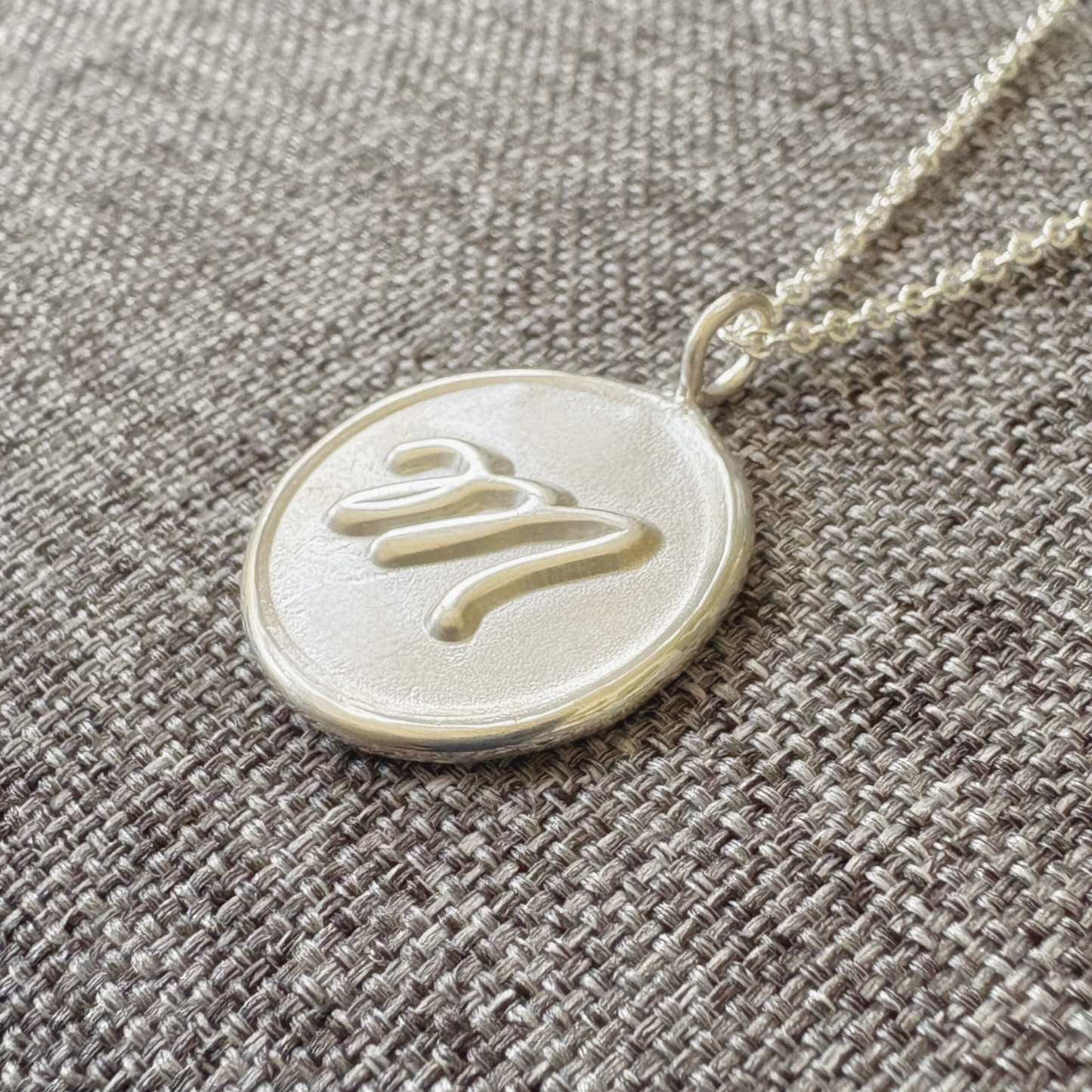 Handcrafted sterling silver initial medallion with satin finish background and polished M on gray textured background