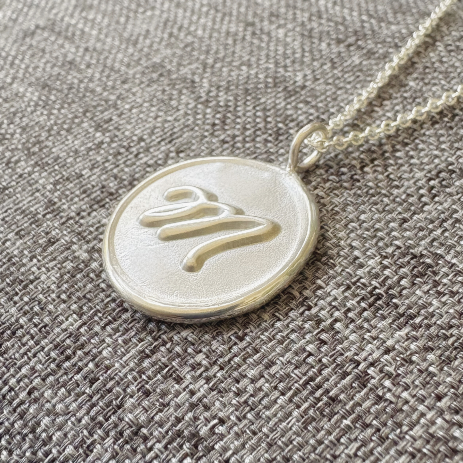 Handcrafted sterling silver initial medallion with satin finish background and polished M on gray textured background