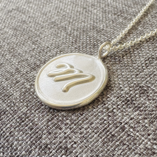 Handcrafted sterling silver initial medallion with satin finish background and polished M on gray textured background